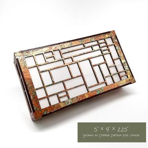 May include: Rectangular wooden box with a copper patina foil finish. The box has a geometric design with rectangular and square cutouts. The dimensions are 12.7cm x 22.9cm x 5.7cm. The text on the image reads "shown in copper patina foil finish".