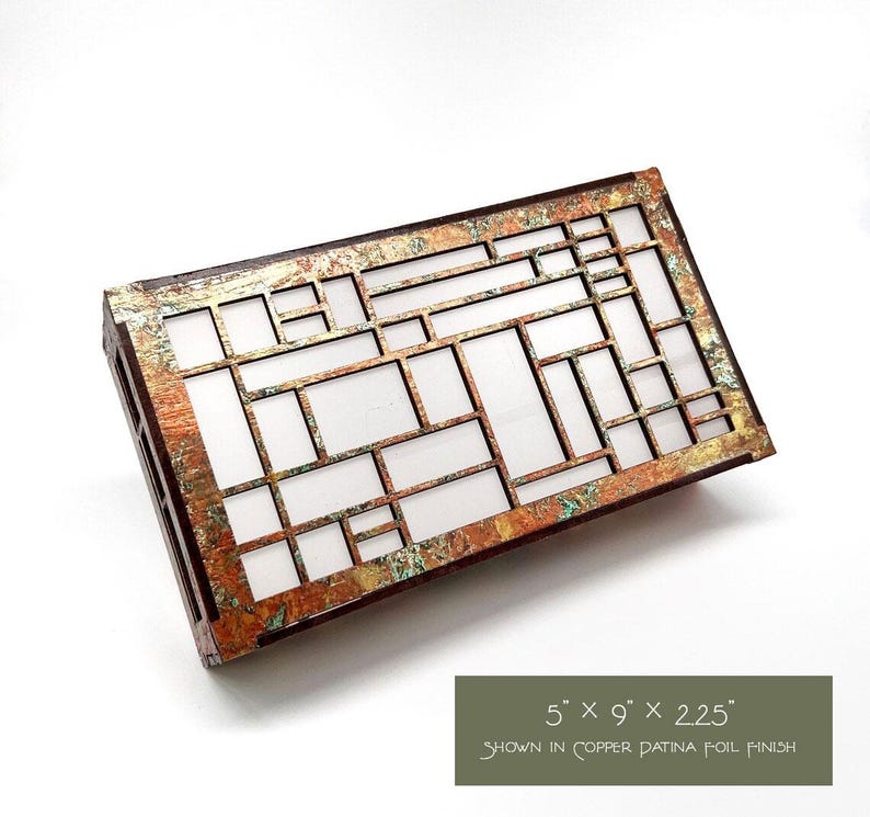 May include: Rectangular wooden box with a copper patina foil finish. The box has a geometric design with rectangular and square cutouts. The dimensions are 12.7cm x 22.9cm x 5.7cm. The text on the image reads "shown in copper patina foil finish".