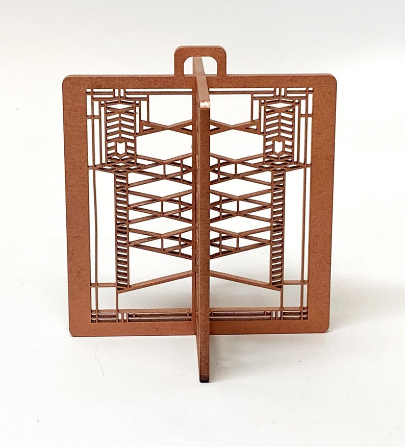 May include: A brown, laser-cut wooden decorative piece with an architectural design. The piece features a rectangular frame with intricate geometric patterns and a handle at the top. The design is symmetrical and stands upright.