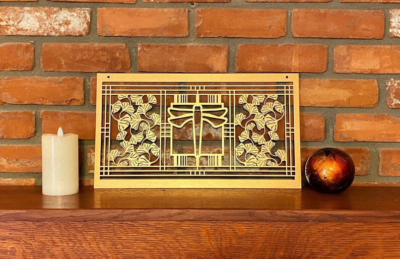 May include: A gold metal wall art piece featuring a dragonfly design and ginkgo leaf accents. The art piece is mounted on a brick wall.