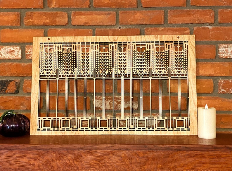 May include: A wooden wall hanging with a geometric design inspired by Frank Lloyd Wright's Prairie School architecture. The design features a repeating pattern of stylized trees and geometric shapes.
