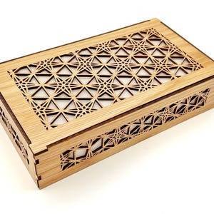 May include: A rectangular wooden box featuring a light brown finish and intricate laser-cut geometric patterns on the lid and sides. The design consists of repeating star and triangle shapes, creating a lattice effect that reveals a white interior.