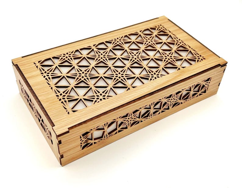 May include: A rectangular wooden box featuring a light brown finish and intricate laser-cut geometric patterns on the lid and sides. The design consists of repeating star and triangle shapes, creating a lattice effect that reveals a white interior.
