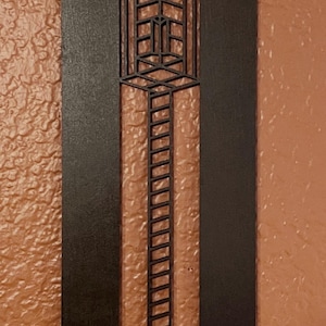 May include: A dark brown, rectangular wall art piece with a geometric design. The art features a central vertical panel with a ladder-like pattern and a series of rectangular shapes. Two small silver rivets are visible at the top.