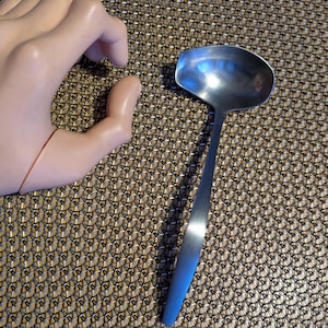 May include: A silver ladle with a long handle. The ladle is on a brown and black patterned surface.