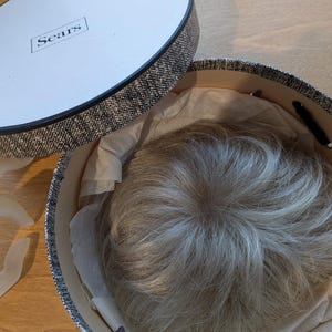 May include: A gray wig in a black and white patterned box with the word "Sears" on the lid.