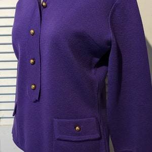 May include: A purple long-sleeved sweater with a collared neckline and gold buttons. The sweater has a patch pocket on the left side.