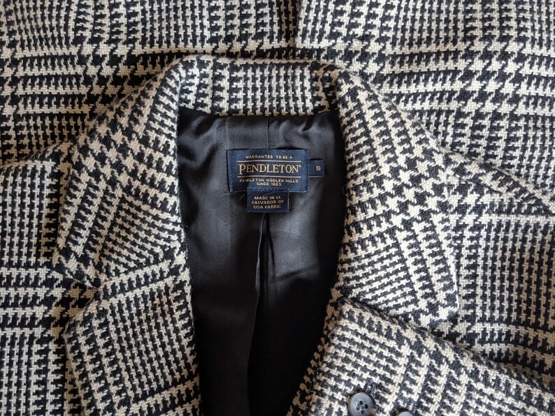 Puede incluir: Primer plano de una blazer con estampado de pata de gallo en blanco y negro. La blazer tiene un forro de sat&eacute;n negro y una etiqueta Pendleton. La blazer tiene dos botones y solapas con muescas. La tela es lana tejida.