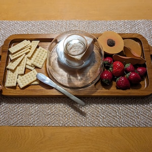 May include: A wooden serving tray with a glass cloche, crackers, strawberries, and a peach slice.