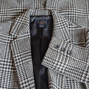 Puede incluir: Un blazer con estampado de pata de gallo en blanco y negro. El blazer tiene solapas con muescas, cierre de dos botones y tres botones en cada pu&ntilde;o. El forro interior es negro y se ve una etiqueta.