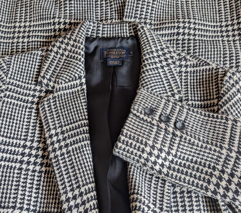 Puede incluir: Un blazer con estampado de pata de gallo en blanco y negro. El blazer tiene solapas con muescas, cierre de dos botones y tres botones en cada pu&ntilde;o. El forro interior es negro y se ve una etiqueta.