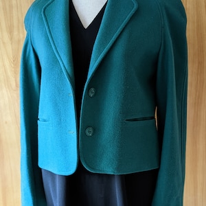 May include: A teal blue blazer with a notched collar, two pockets, and three buttons. The blazer is on a mannequin and has long sleeves.