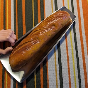 May include: A long loaf of bread on a silver serving tray. The tray is on a striped fabric background.