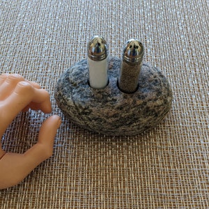 May include: Two salt and pepper shakers in a stone holder. The shakers are silver with black and white tops. The stone holder is gray and has a rough texture.