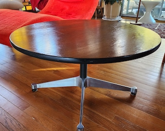 May include: A round coffee table with a dark brown wooden top and a black edge. The table has a silver, star-shaped base with four legs. The table is set on a hardwood floor.