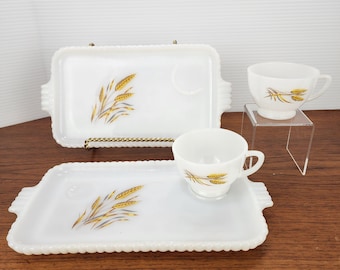May include: A white vintage serving set featuring two rectangular trays and two teacups. Each piece has a gold wheat stalk design and a beaded edge. The teacups are on a clear stand. The trays measure approximately 10 inches long.