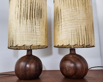 May include: Pair of mid-century modern table lamps. Each lamp features a round, dark wood base and a cylindrical shade with a cream-colored background and vertical brown lines. The shades are trimmed with black stitching.