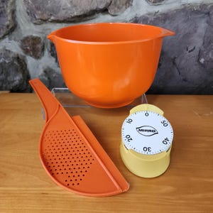 May include: Orange mixing bowl, orange colander with a handle, and a yellow kitchen timer with a white face that reads "MIRRO" and has numbers from 0 to 60.