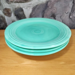 May include: Three turquoise blue ceramic dinner plates stacked on top of each other. The plates have a ridged design around the edge.
