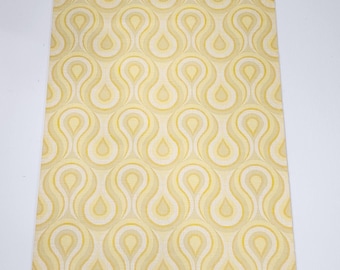 May include: A roll of vintage wallpaper with a repeating pattern of yellow and cream-colored teardrop shapes. The wallpaper is displayed vertically with a pencil sharpener at the top and bottom. The pattern has a retro, mid-century modern aesthetic.