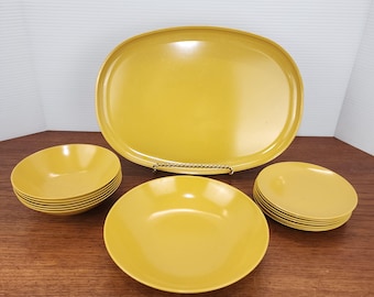 May include: A vintage yellow serving set featuring an oval platter, several small bowls, and plates. The set is made of a durable material and is arranged on a wooden surface. The color is a bright, sunny yellow.