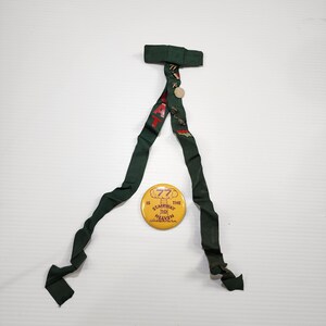 May include: Dark green necktie with a floral pattern and a round button. A yellow button with the text "IS THE STAIRWAY TO HEAVEN" is also present. The tie is made of a soft, flowing fabric.