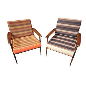 May include: Two mid-century modern armchairs with striped fabric upholstery. The chairs have wooden frames and legs with brass accents.
