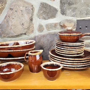 May include: A collection of brown and white glazed pottery dishes, bowls, and mugs. The set includes a large serving dish, a smaller bowl, a pitcher, and several mugs. The pottery is decorated with a brown and white glaze, and the pieces are all in good condition.