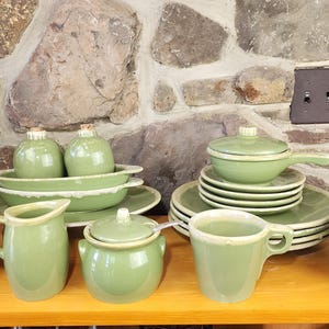 May include: A set of green ceramic kitchenware, including a teapot, creamer, sugar bowl, serving dishes, and bowls. The set features a light green glaze with a white rim.