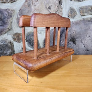 May include: A wooden napkin holder with a natural wood finish. The holder has a rectangular base and a raised top with a curved design. The holder is made of solid wood and has a rustic look.