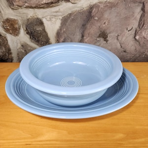 May include: A light blue ceramic bowl with a matching plate. The bowl has a slightly rounded rim and a smooth, glazed finish. The plate has a scalloped edge and a similar glazed finish.