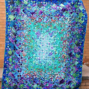 May include: A large rectangular quilt featuring a vibrant patchwork design with a gradient colour scheme transitioning from deep blue and purple at the edges to a bright turquoise and white centre, composed of numerous small fabric squares.