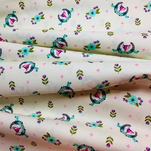 May include: White fabric with a repeating pattern of blue and green floral wreaths, pink flowers, and small green leaves. The wreaths contain a pink and blue trophy.