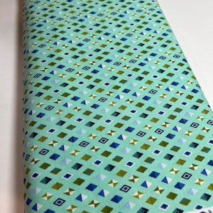 May include: A teal fabric with a repeating pattern of small blue, green, and white geometric shapes. The fabric has the text "Slow & Steady by TULA PINK" printed on the bottom edge.