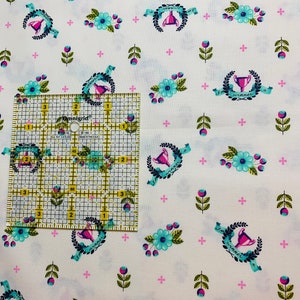 May include: White fabric with a repeating pattern of blue and green floral sprigs, pink plus signs, and a trophy with a pink ribbon and the text "I'm a winner".