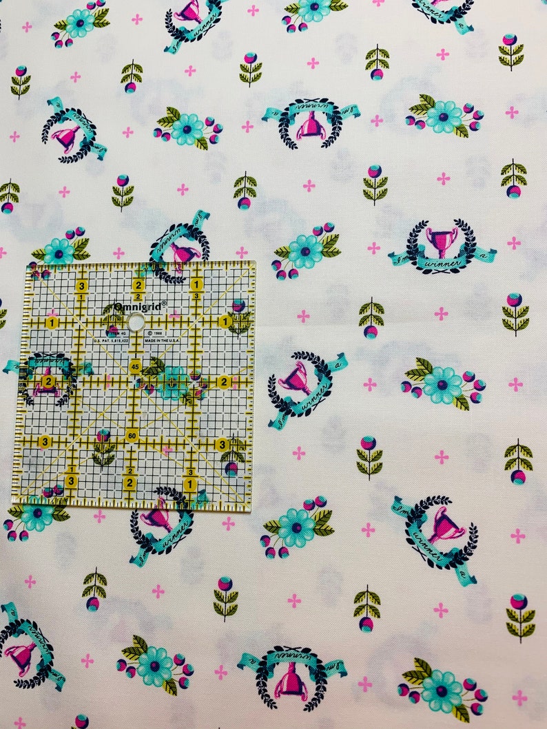 May include: White fabric with a repeating pattern of blue and green floral sprigs, pink plus signs, and a trophy with a pink ribbon and the text "I'm a winner".