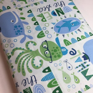 May include: White fabric with a green, blue, and white sea creature pattern. The fabric has the text "And the sea" repeated on it.