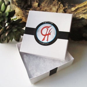 May include: White gift box with a black ribbon and a logo that says "Craft Bombells Handcrafted by Kim". The box is open and has white tissue paper inside.