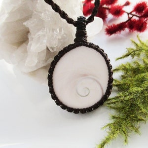 May include: A white shell pendant with a spiral pattern, set in a brown macrame cord necklace.