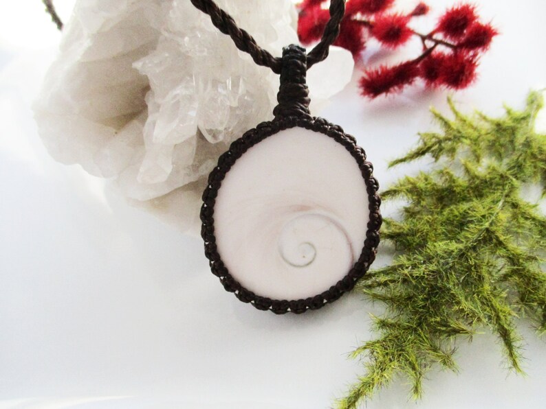 May include: A white shell pendant with a spiral pattern, set in a brown macrame cord necklace.