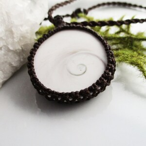 May include: A brown crocheted cord necklace with a white and brown nautilus shell pendant.