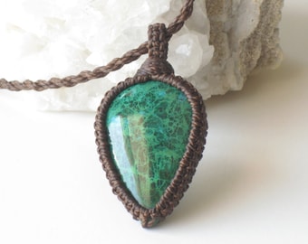 May include: A green malachite gemstone pendant with brown macrame cord. The pendant is in the shape of a teardrop and has a natural, organic look.