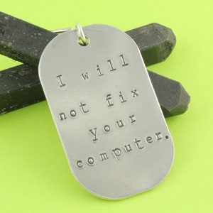 May include: A silver metal keychain tag with the text "I will not fix your computer." The tag is on a green surface.