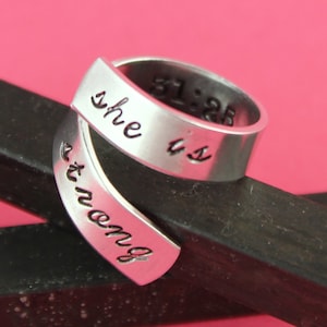 May include: A silver ring with the words "She is" and "not wrong" engraved on it. The ring is wrapped around a black surface.