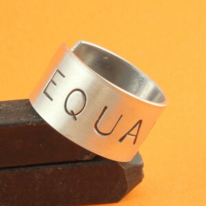 May include: A silver ring with the word "EQUAL" engraved on it. The ring is open ended and can be adjusted to fit different finger sizes.