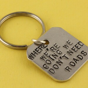 May include: Silver keychain with a square tag that reads "WHERE WE'RE GOING WE DON'T NEED ROADS".