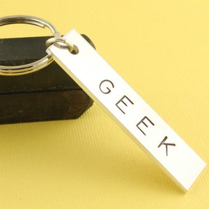 May include: Silver keychain with a rectangular tag that says "GEEK" in all caps.