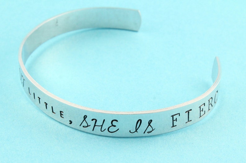 Peut inclure: Bracelet en argent avec l'inscription "She is fierce, little" grav&eacute;e sur la bande.