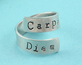 May include: A silver ring with the words "Carpe Diem" engraved on it. The ring is a wrap-around style, with the words on two separate bands.
