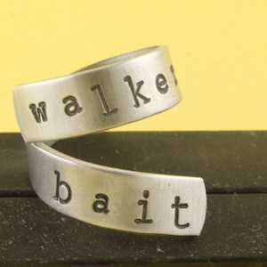 May include: A silver ring with the words "walk it" engraved on it. The ring is made of two bands that are twisted together.